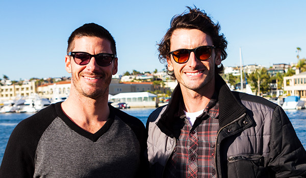 2 guys smiling for camera with harbor behind them