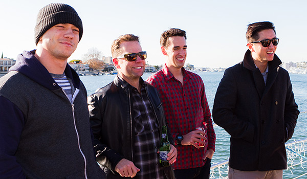 4 guys with houses across the ocean visible behind them